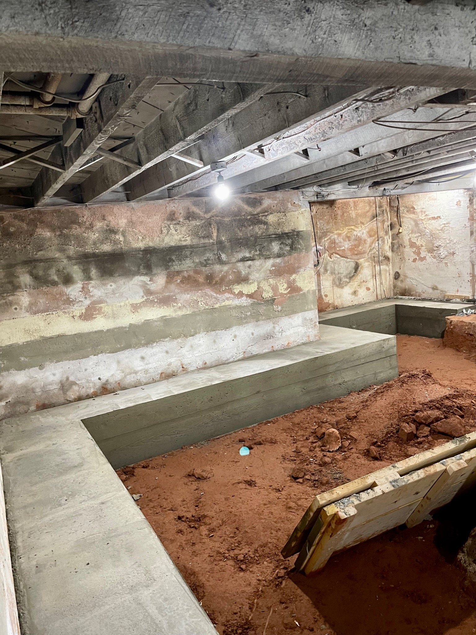 Reinforced concrete bench footing constructed to allow a basement floor to be lowered